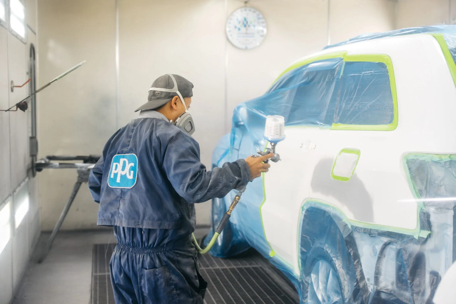 Paint technician spraying PPG waterborne basecoat along the side of a masked white SUV