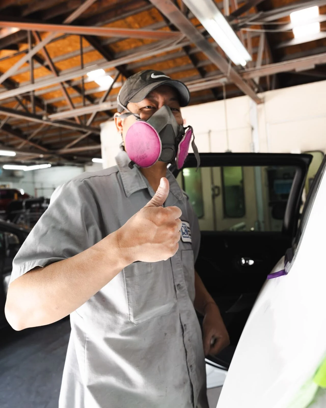 Renewal Body Works paint technician giving a thumbs up beside the paint booth